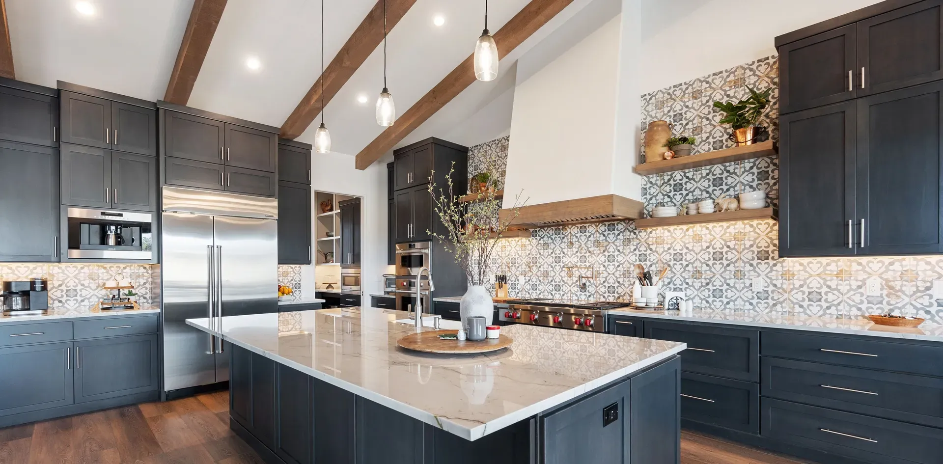 A refaced kitchen with navy shaker cabinets, a white marble island and a patterned tile backsplash under a vaulted ceiling with exposed wood beams